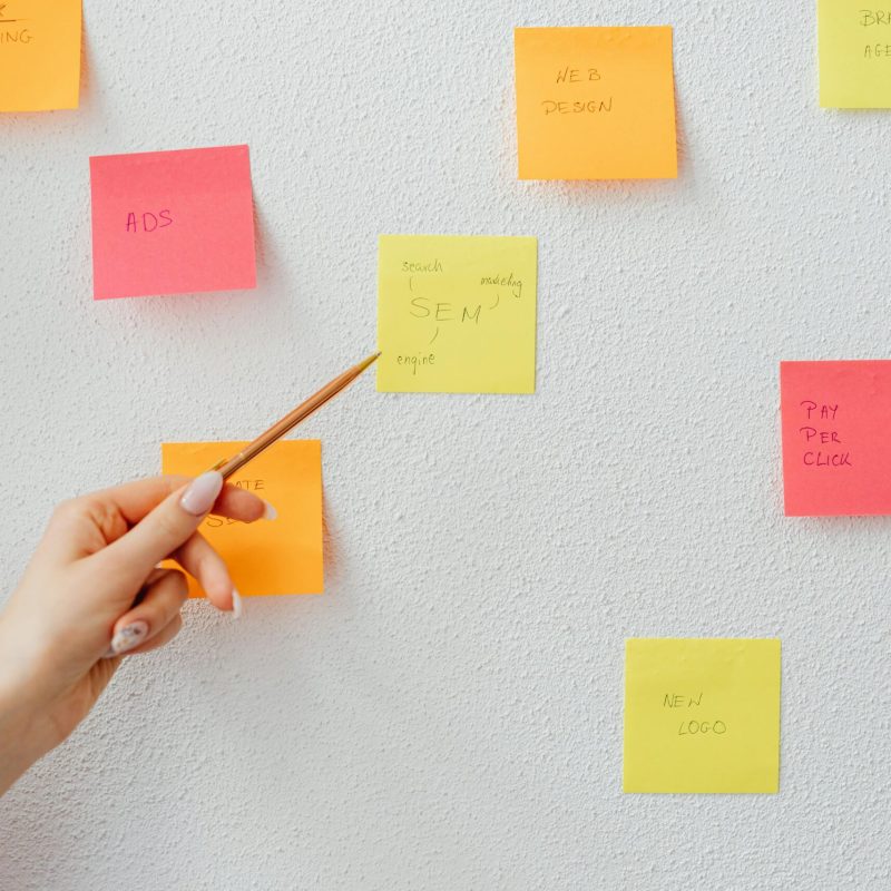 Hand pointing at colorful sticky notes with business concepts on a wall.